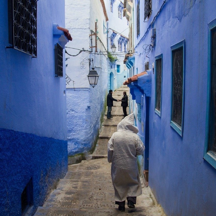 Man with djelleba strolling through the narrow streets of the blue medina of Chefchaouen.